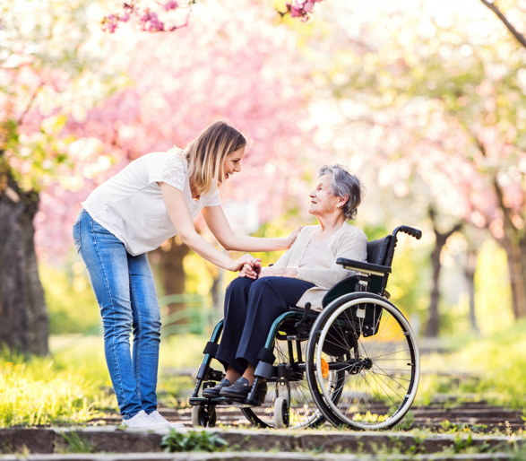Ältere Großmutter im Rollstuhl mit Enkelin im Frühling Natur