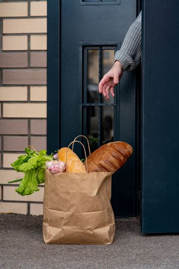 Quarantäne kontaktlosen Lieferbanner mit Hand und geliefertem Papiersack in der Nähe der Tür. Hauseingang mit gelieferter Tasche. Maßnahmen zur Verhütung von Epidemien durch Coronavirus.